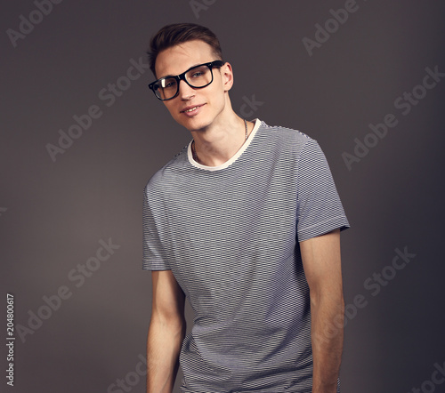 Fashion smiling man posing in trendy glasses in strip casual shirt and white jeans on grey background. Toned closeup portrait with empty copy space © nastia1983