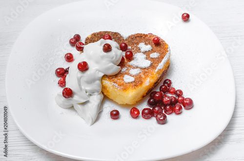 Freshly baked curd on the plate with cranberry and powdered sugar and sour cream on white wooden table background.