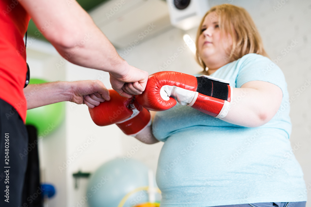 Low angle portrait of young obese woman fist bumping with personal fitness coach during training in gym, copy space