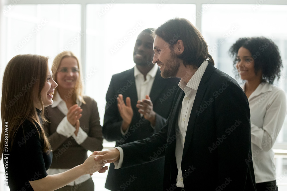 Smiling boss shaking hand of cheerful happy female employee promoting rewarding excited worker or congratulating partner with achievement while team applauding, appreciation handshake, recognition Smiling boss shaking hand of cheerful happy female employee promoting rewarding excited worker or congratulating partner with achievement while team applauding, appreciation handshake, recognition
