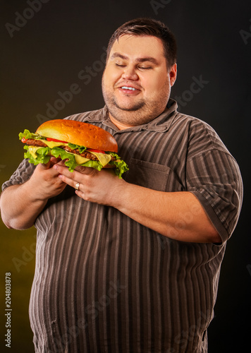 Man eating fast food hamberger. Fat person in large size shirt made great huge hamburger. How to dress well as overweight people concept. Obesity is harmful to health.