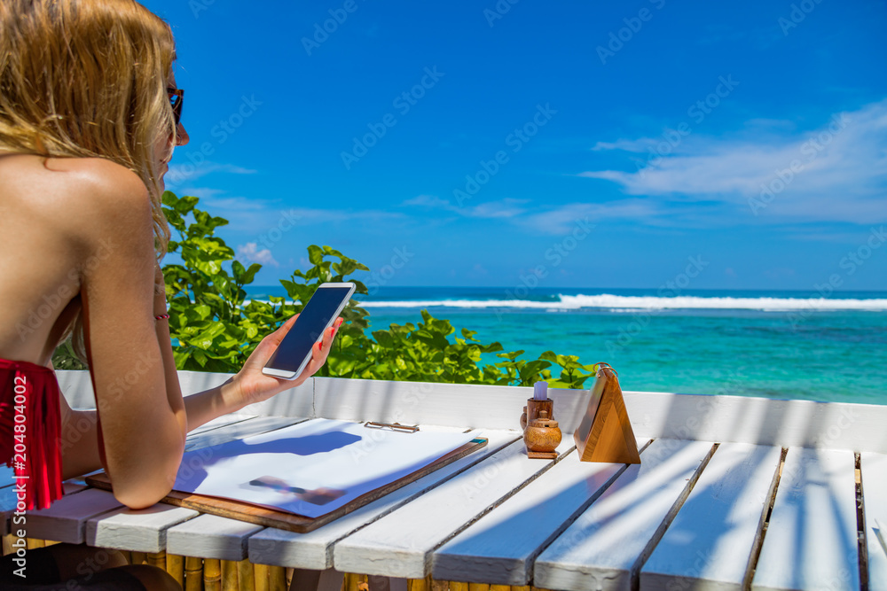 Girl using cellphone in the restaurant on a exotic tropical beach.