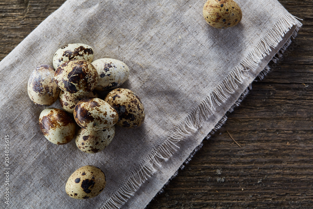 Quail eggs arranged in pyramid on a napkin with boxwood branches over a wooden table, close-up, selective focus. Quail eggs arranged in pyramid on a napkin with boxwood branches over a wooden table, close-up, selective focus.