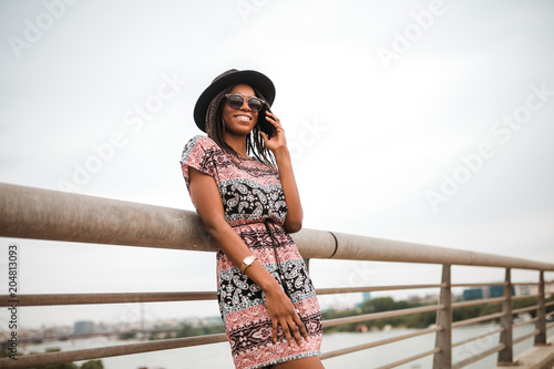 Young african american woman standing next to bridge railing above river water © Nebojsa