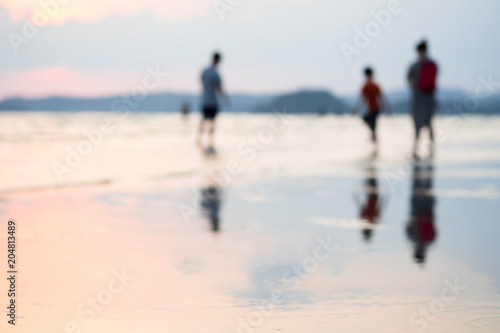 Blurred background of people enjoying life on summer beach in sunset.