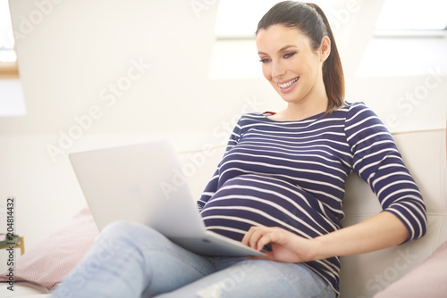Pregnant woman using laptop while lying on couch and relaxing at hom