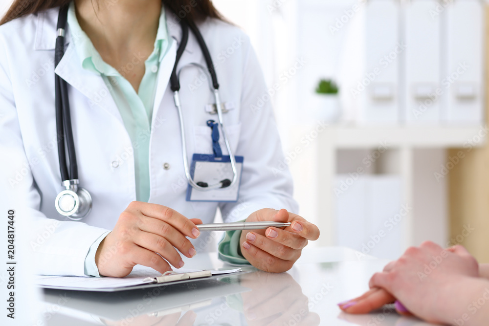 Doctor and patient talking while sitting at the desk in hospital office, closeup of human hands. Medicine and health care concept Doctor and patient talking while sitting at the desk in hospital office, closeup of human hands. Medicine and health care concept