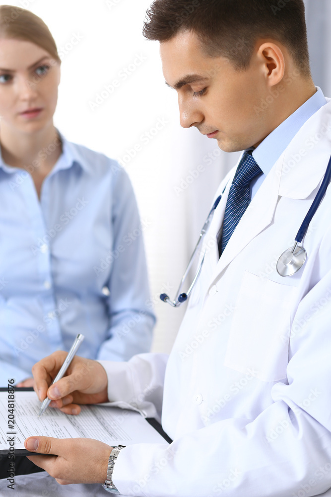 Male doctor holding application form while consulting female patient in hospital office. Perfect service in medicine and healthcare concept Male doctor holding application form while consulting female patient in hospital office. Perfect service in medicine and healthcare concept