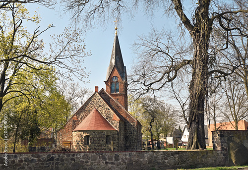View of a village church near Berlin. In the foreground there is a wall of fieldstones.