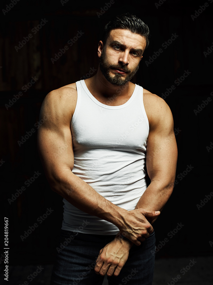 A strong, a serious, muscular man in a white t-shirt is worth and looks in camera. He's got the beard on the face and different emotions A strong, a serious, muscular man in a white t-shirt is worth and looks in camera. He's got the beard on the face and different emotions