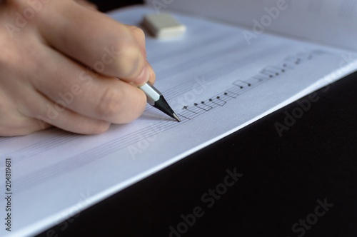 Side view of the hand writing the music notes with pencil. The concept of the music creating, composing, note writing, music art.
