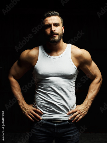 A strong  a serious  muscular man in a white t-shirt is worth and looks in camera. He s got the beard on the face and different emotions