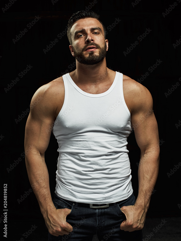 A strong, a serious, muscular man in a white t-shirt is worth and looks in camera. He's got the beard on the face and different emotions A strong, a serious, muscular man in a white t-shirt is worth and looks in camera. He's got the beard on the face and different emotions