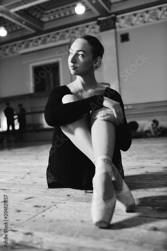 portrait of a cute young ballerina sitting on a wooden floor in a ballet class