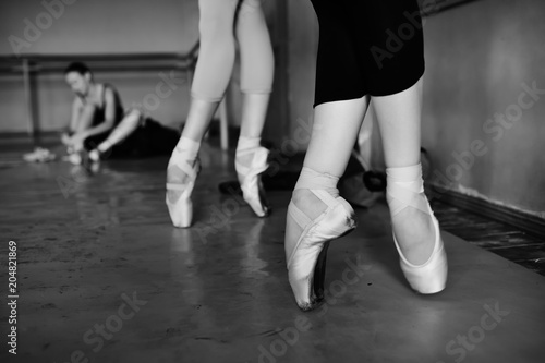 feet of young ballerinas in pointe shoes close-up against the backdrop of a ballet class