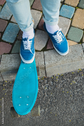 Hipster in blue canvas shoes standing on the pavement with blue plastic penny skateboard. The concept of city travelling, vlogging, modern lifestyle photo