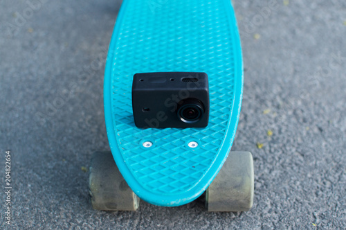 Action camera in silicon case on the blue plastic penny skateboard. Front view. The concept of city travelling, vlogging, modern lifestyle photo