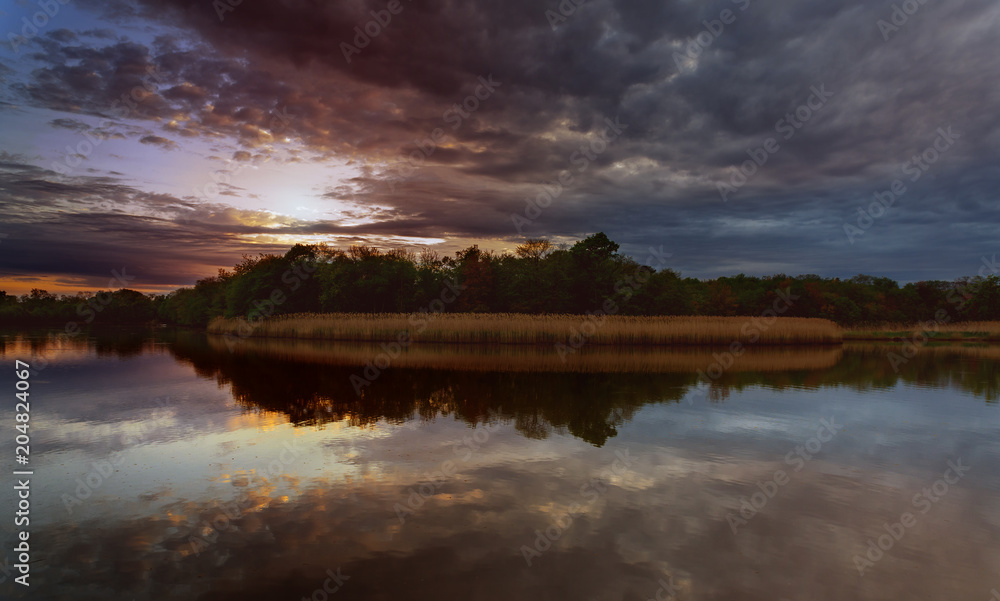 Fototapeta premium Beautiful sunset over lake with reflection in water, majestic clouds in the sky Toned Image