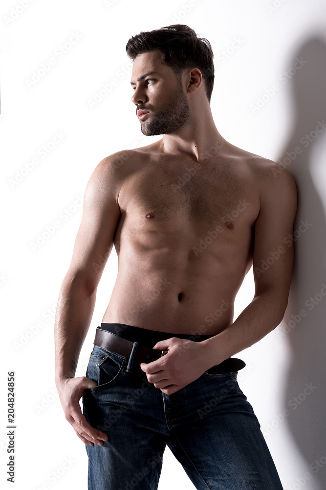 Muscular male is standing and leaning on white wall. He is looking aside pensively Muscular male is standing and leaning on white wall. He is looking aside pensively