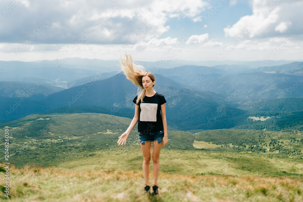 Odd strange unusual young girl playing with hair in mountains. Tilt shft mood portrait of long haired blonde babe outdoor. State of mind.  Female hiker relaxing at nature. Beautiful landscape view.