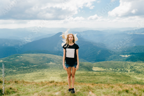 Odd strange unusual young girl playing with hair in mountains. Tilt shft mood portrait of long haired blonde babe outdoor. State of mind. Female hiker relaxing at nature. Beautiful landscape view.