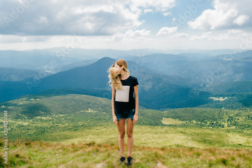 Odd strange unusual young girl playing with hair in mountains. Tilt shft mood portrait of long haired blonde babe outdoor. State of mind. Female hiker relaxing at nature. Beautiful landscape view.