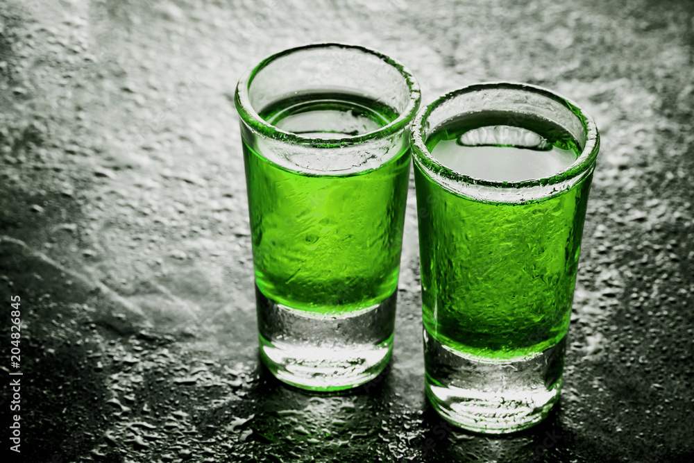 Two glass vodka shots with abstract color green alcohol poured inside.  Weekend alcohol party background. Stock Photo