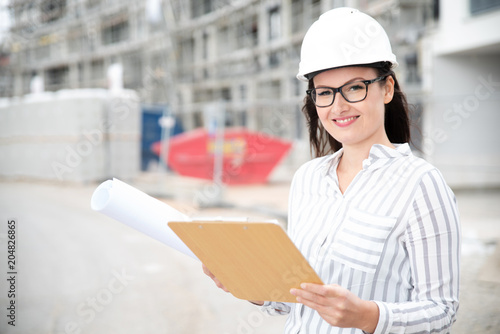 Frau mit Klemmbrett und Plänen auf einer Baustelle 