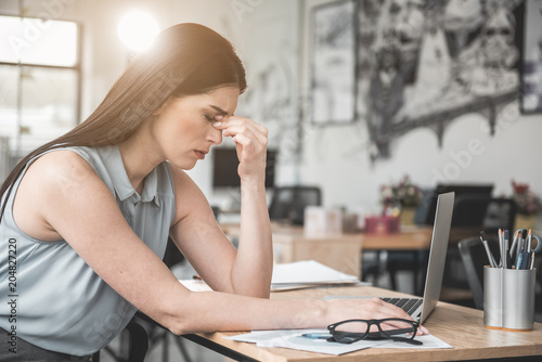 Side view sad businesswoman feeling pain in eyes while typing in laptop in office. Sick worker at labor concept