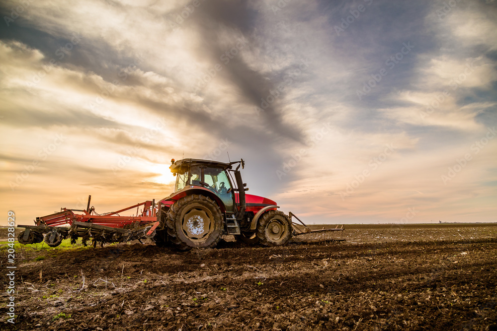 Obraz premium Tractor cultivating field at spring