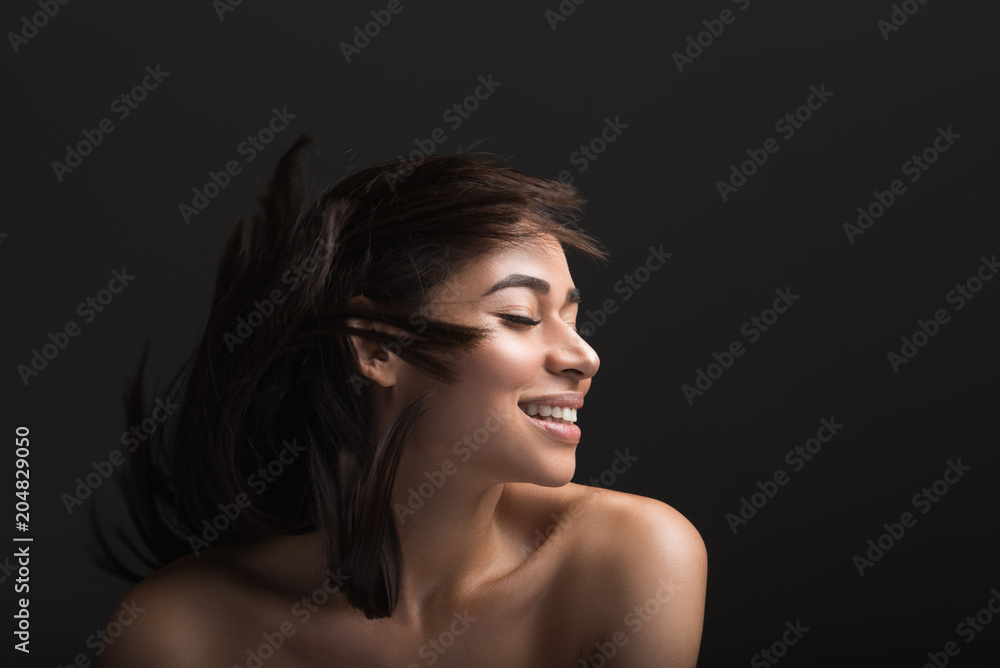 Content female person waving her treated hairdo and laughing. Copy space in right side. Isolated on black background Content female person waving her treated hairdo and laughing. Copy space in right side. Isolated on black background