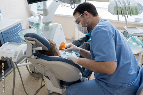 Portrait of dentist treating teeth of little boy sitting in dental chair at modern clinic