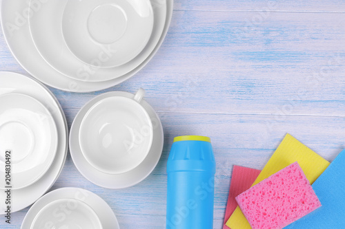 Cleaning powder and washcloths with white plates and cups on a blue wooden background photo