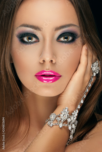 beautiful young girl with make-up of glossy pink lips with long eyelashes and a jewelry bracelet with stones on her hand