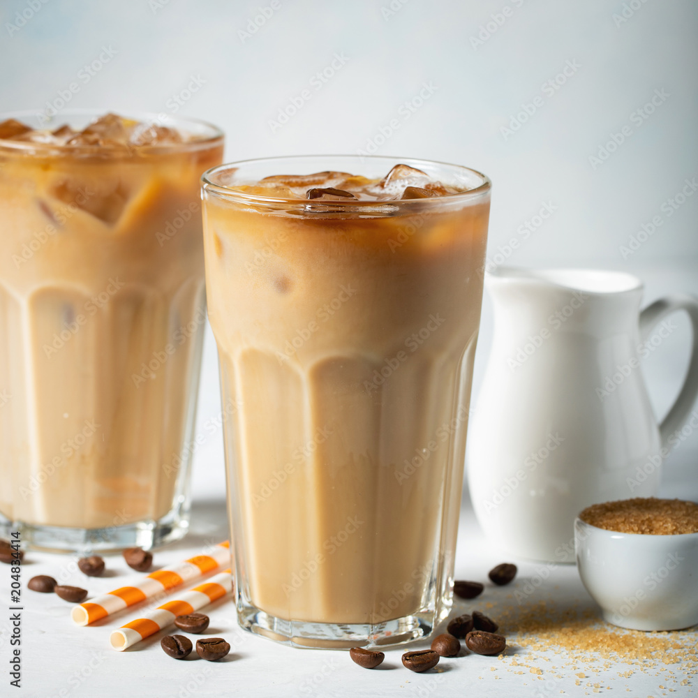 Ice coffee in a tall glass with cream poured over and coffee beans. Cold summer drink on a light blue background Ice coffee in a tall glass with cream poured over and coffee beans. Cold summer drink on a light blue background