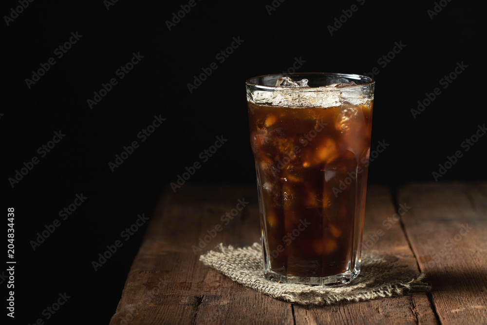 Ice coffee in a tall glass over and coffee beans on a old rustic wooden table. Cold summer drink on a dark background with copy space Ice coffee in a tall glass over and coffee beans on a old rustic wooden table. Cold summer drink on a dark background with copy space