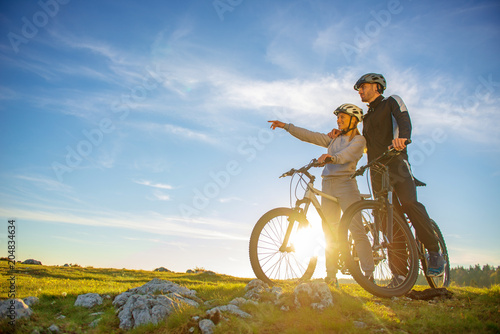 Biker couple with mountain bike pointing in distance at countryside