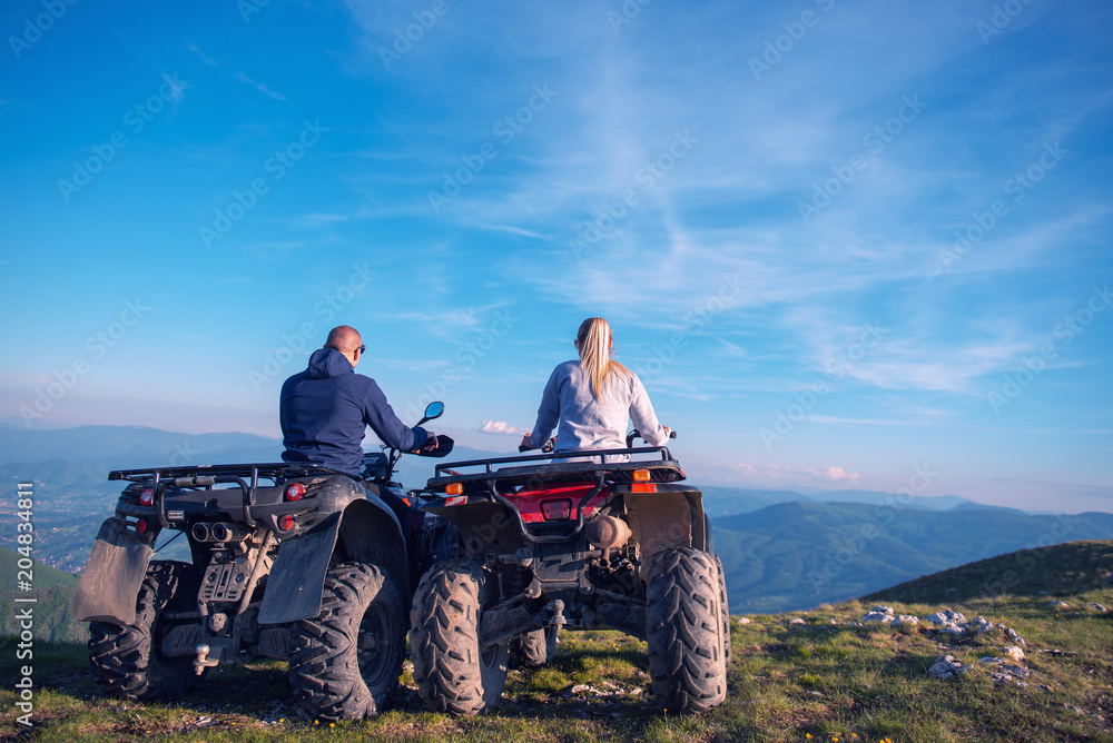 Obraz premium Rear view of young pair near atv. Man is showing something in distance to her girlfriend.