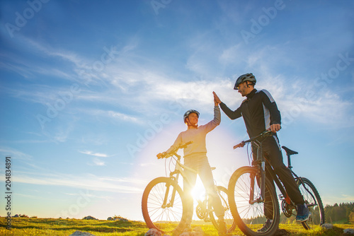 happy couple goes on a mountain road in the woods on bikes with helmets giving each other a high five