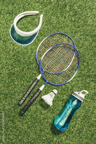 top view of badminton equipment, water bottle and cap on green grass
