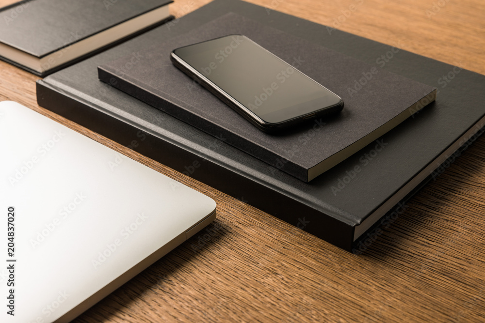 close up view of laptop, pile of black notebooks and smartphone on wooden tabletop close up view of laptop, pile of black notebooks and smartphone on wooden tabletop