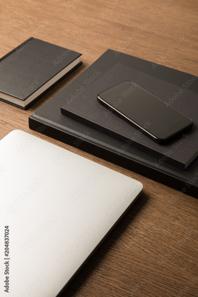 close up view of laptop, pile of black notebooks and smartphone on wooden tabletop close up view of laptop, pile of black notebooks and smartphone on wooden tabletop