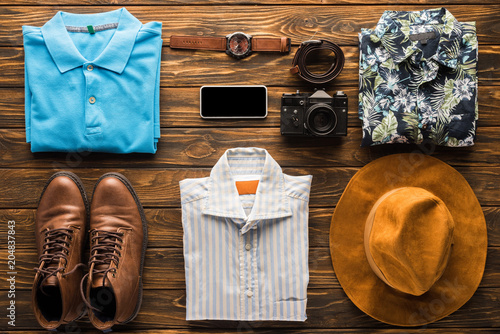 top view of stylish clothes with film camera and smartphone on wooden surface, travel concept