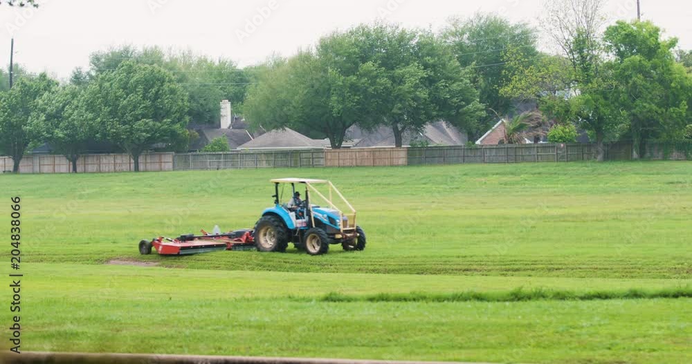 Close shot of large tractor cutting the grass of a large detention pond surrounded by suburban neighborhoods 4k Close shot of large tractor cutting the grass of a large detention pond surrounded by suburban neighborhoods 4k
