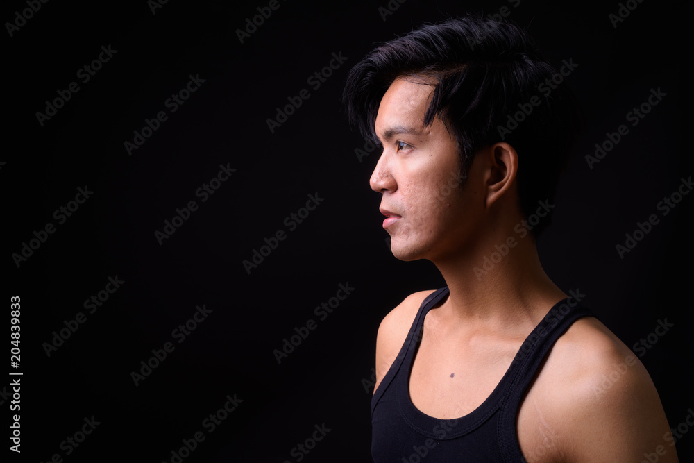 Naklejka premium Young handsome Asian man against black background