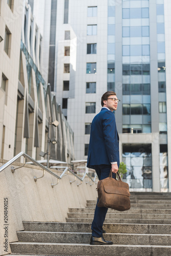 handsome businessman in stylish suit with leather briefcase going up stairs