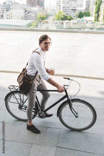 Fototapeta Naklejka Na Ścianę i Meble -  high angle view of attractive young man with paper cup of coffee on vintage bicycle
