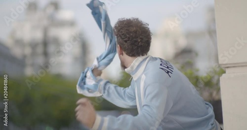 Happy Argentinian football supporter waving jersey while celebrating victory in balcony