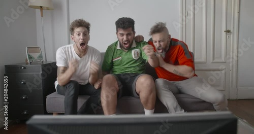 Cheerful Mexican football supporters celebrating goal while watching football match on television at home