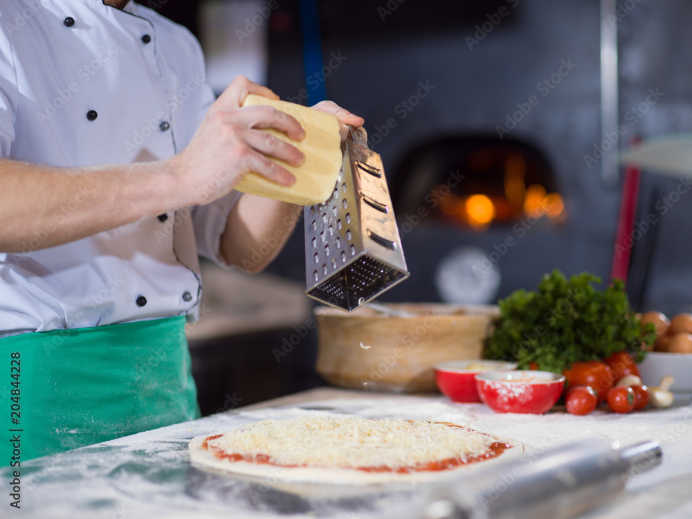 chef sprinkling cheese over fresh pizza dough